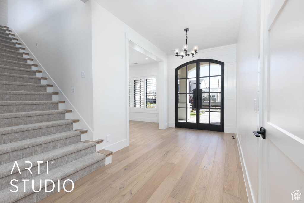 Foyer with french doors, a chandelier, baseboards, light wood finished floors, and stairway