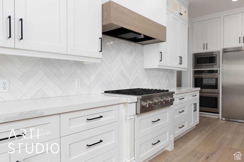 Kitchen with built in appliances, premium range hood, white cabinetry, and backsplash