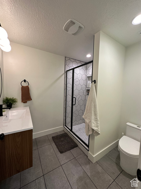 Bathroom with a textured ceiling, tile patterned floors, a stall shower, toilet, and double vanity