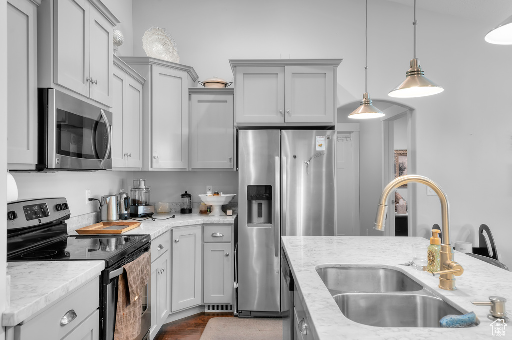 Kitchen with appliances with stainless steel finishes, a sink, decorative light fixtures, light stone countertops, and gray cabinets