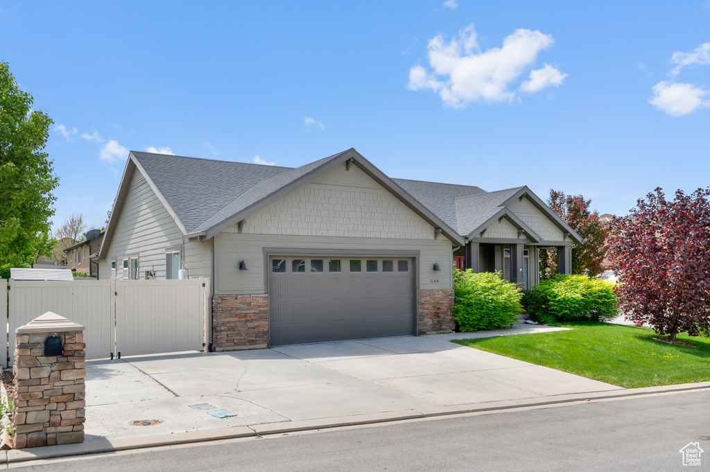 Craftsman inspired home with a garage, roof with shingles, driveway, a gate, and stone siding
