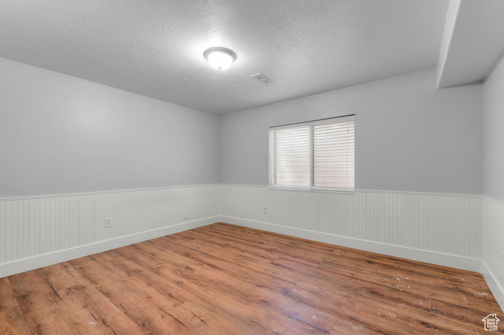 Unfurnished room with hardwood / wood-style flooring, wainscoting, and a textured ceiling
