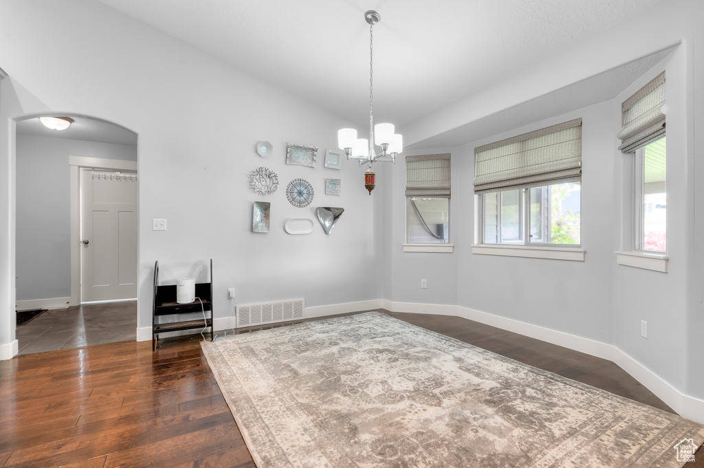 Unfurnished dining area featuring arched walkways, dark wood finished floors, baseboards, and a chandelier