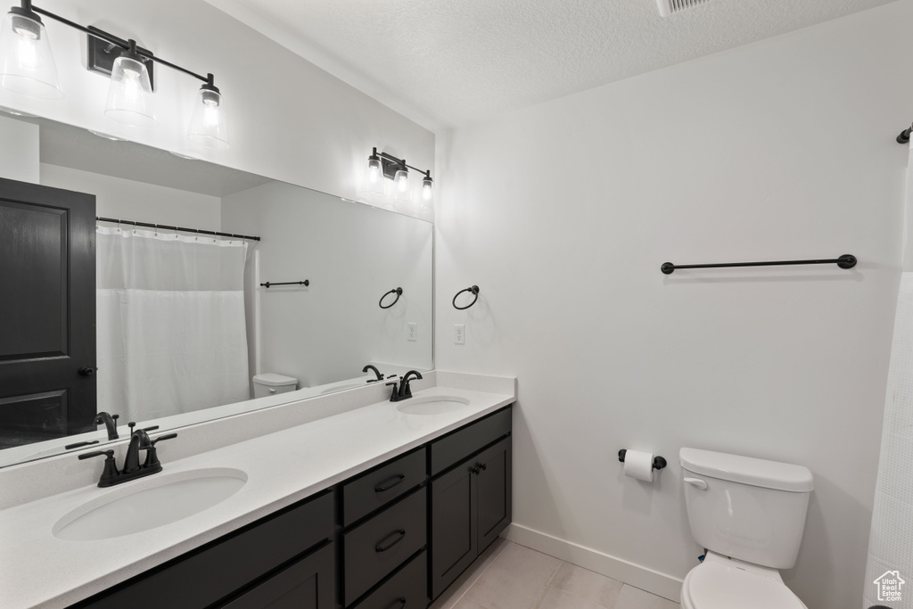 Bathroom with toilet, baseboards, double vanity, tile patterned floors, and a textured ceiling