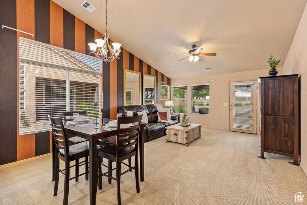 Dining room with vaulted ceiling, light colored carpet, ceiling fan, a chandelier, and baseboards