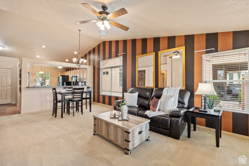 Living room with healthy amount of natural light, lofted ceiling, ceiling fan, light colored carpet, and a chandelier