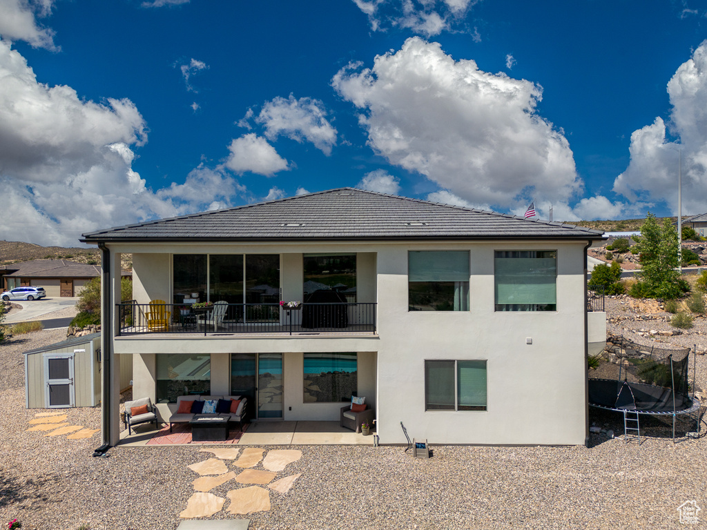 Back of house with outdoor lounge area, a trampoline, a patio, stucco siding, and a balcony