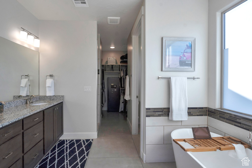Full bathroom with a spacious closet, vanity, tile patterned flooring, a freestanding tub, and baseboards