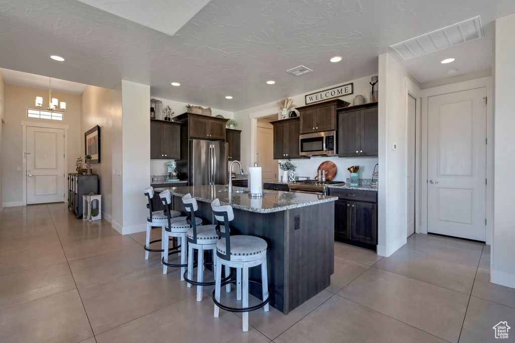 Kitchen featuring appliances with stainless steel finishes, a kitchen bar, dark brown cabinetry, a sink, and recessed lighting