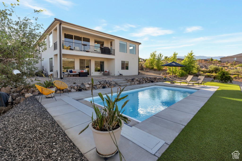 Back of property with a balcony, a patio area, stucco siding, an outdoor living space, and a yard