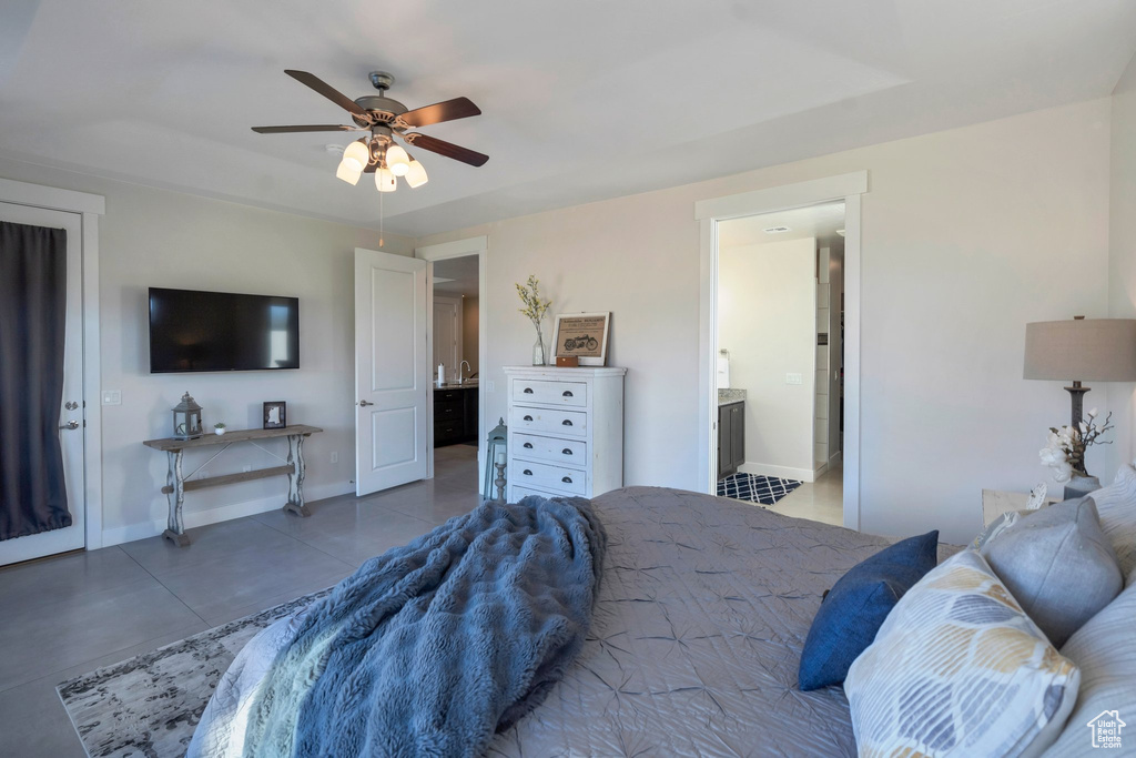 Tiled bedroom featuring baseboards, a ceiling fan, ensuite bath, and a tray ceiling