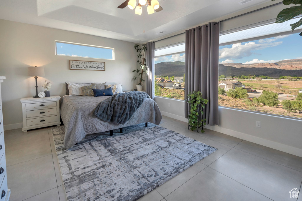 Bedroom featuring a raised ceiling, light tile patterned floors, a mountain view, baseboards, and ceiling fan