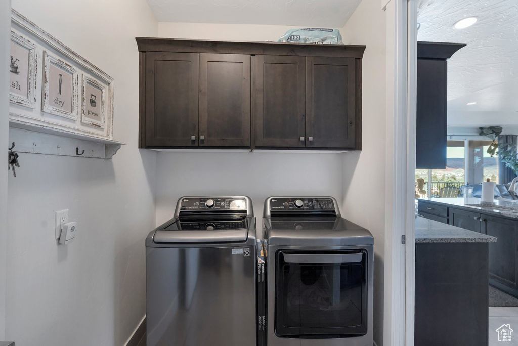 Clothes washing area featuring washing machine and dryer, cabinet space, and baseboards