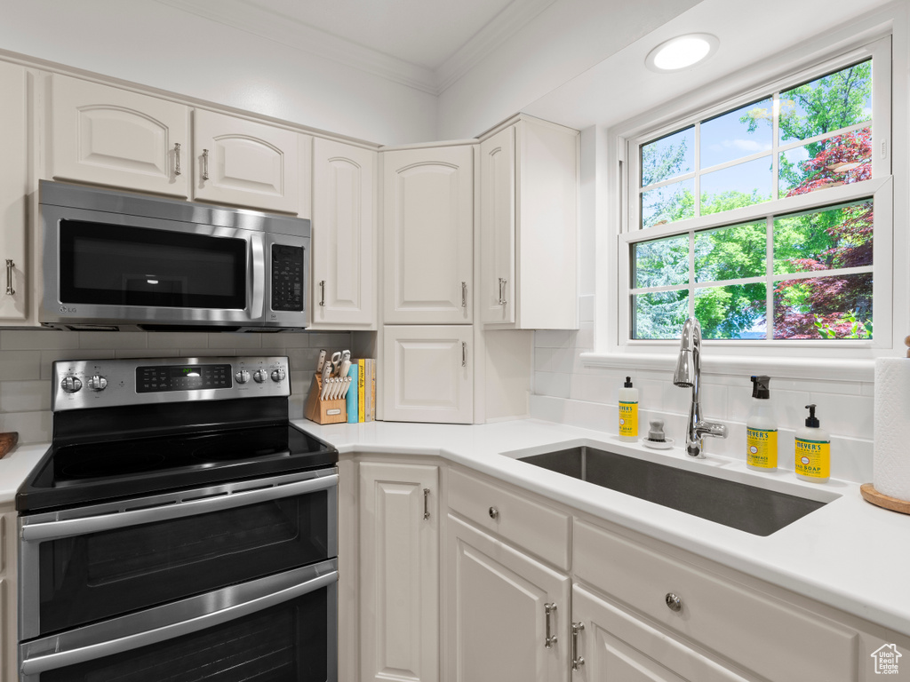 Kitchen featuring appliances with stainless steel finishes, a sink, ornamental molding, decorative backsplash, and white cabinets