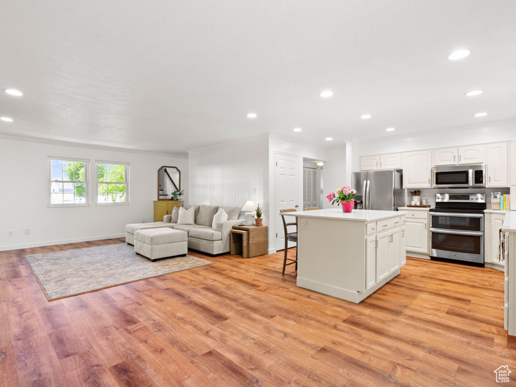 Kitchen featuring stainless steel appliances, a center island, white cabinets, open floor plan, and light wood-style floors