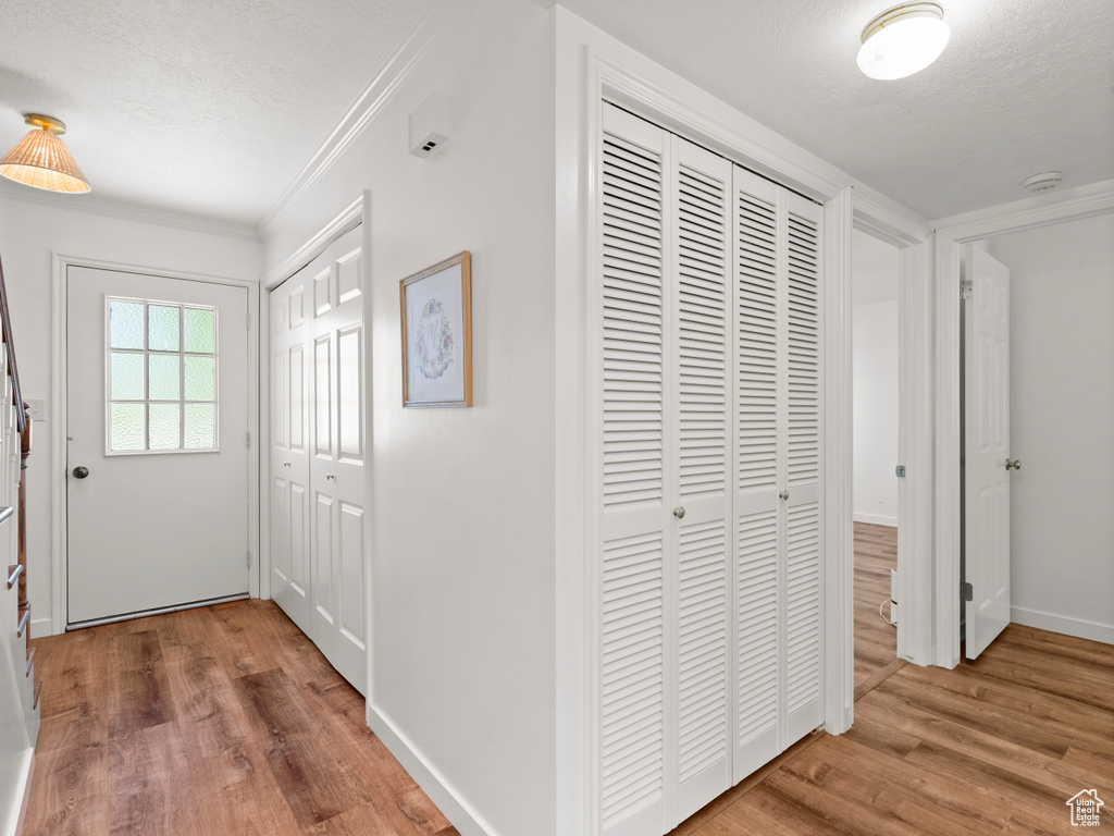 Hallway featuring wood finished floors, a textured ceiling, crown molding, and baseboards