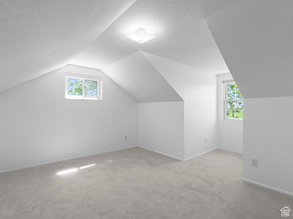 Bonus room with vaulted ceiling, light carpet, baseboards, and a textured ceiling