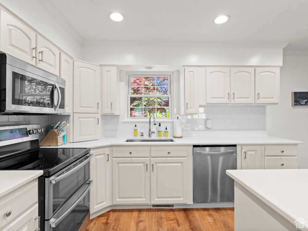 Kitchen with appliances with stainless steel finishes, a sink, crown molding, backsplash, and white cabinetry