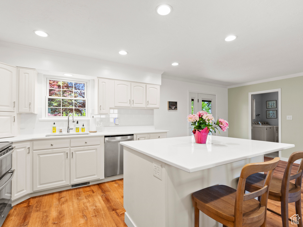 Kitchen with a sink, appliances with stainless steel finishes, a kitchen bar, ornamental molding, and a kitchen island