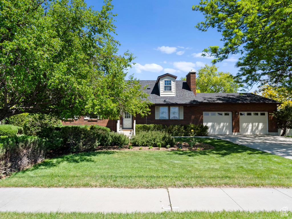 View of front of home with a chimney, a garage, driveway, and a front lawn