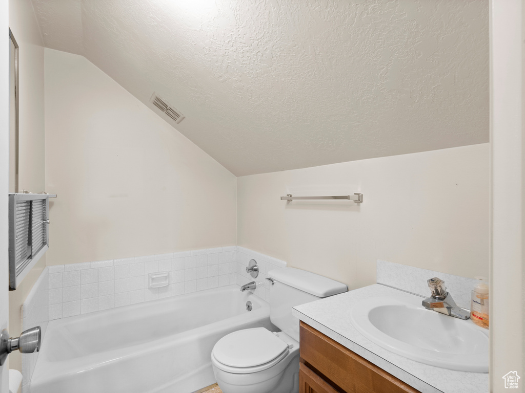 Bathroom with lofted ceiling, a garden tub, a textured ceiling, toilet, and vanity