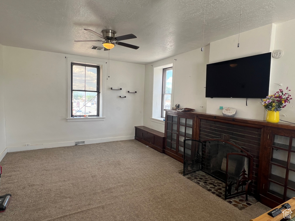 Living area with a textured ceiling, carpet flooring, ceiling fan, and baseboards