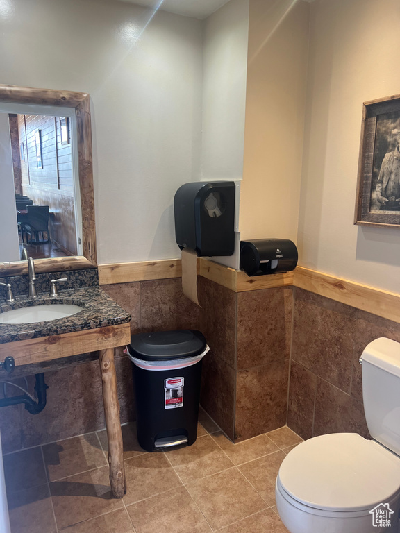 Half bath featuring tile walls, toilet, wainscoting, a sink, and tile patterned flooring