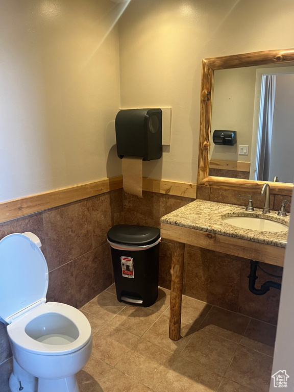Bathroom with tile walls, toilet, a wainscoted wall, and a sink