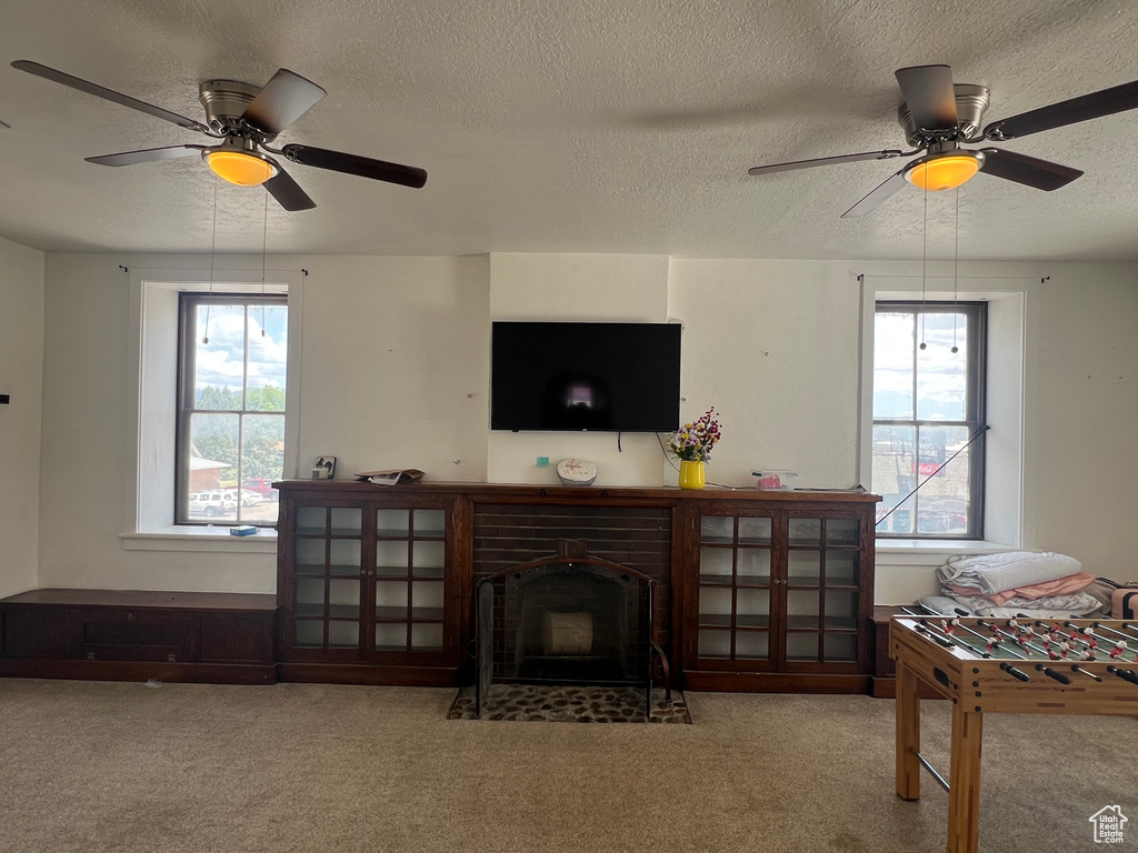 Living area with ceiling fan, a textured ceiling, carpet flooring, and a fireplace with flush hearth