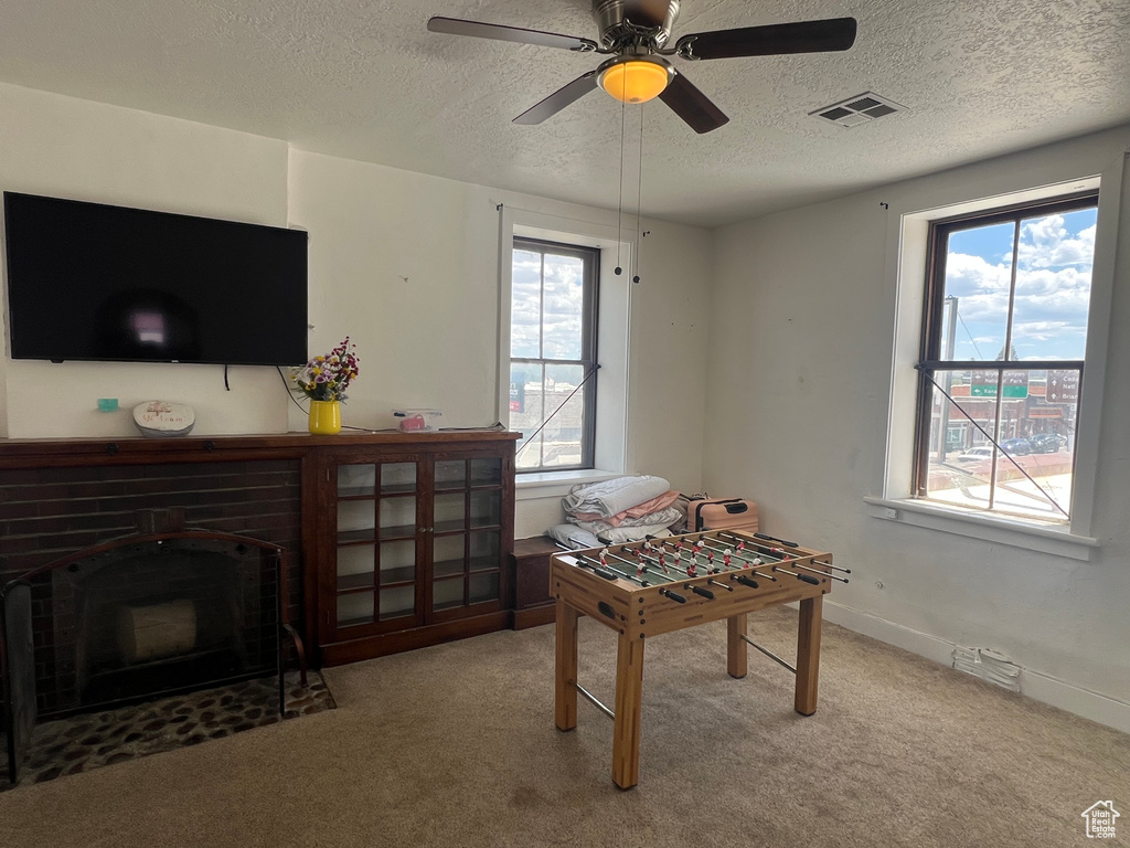 Recreation room featuring carpet, a textured ceiling, a ceiling fan, baseboards, and a brick fireplace