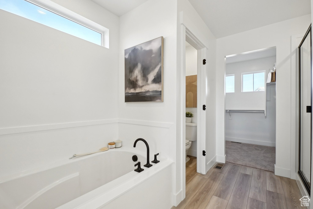 Bathroom featuring healthy amount of natural light, a bath, toilet, and wood finished floors