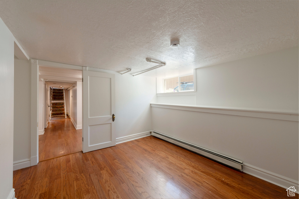 Additional living space with a baseboard radiator, wood finished floors, a textured ceiling, and baseboards