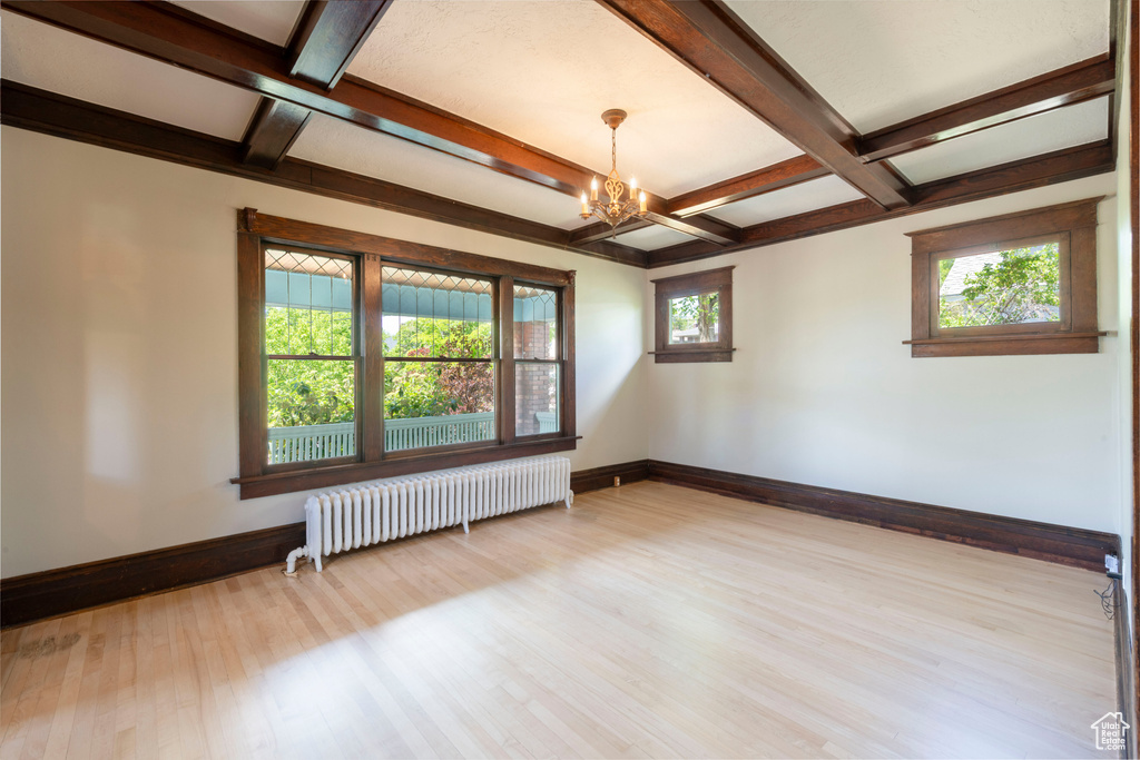 Empty room featuring radiator, coffered ceiling, a chandelier, wood finished floors, and baseboards