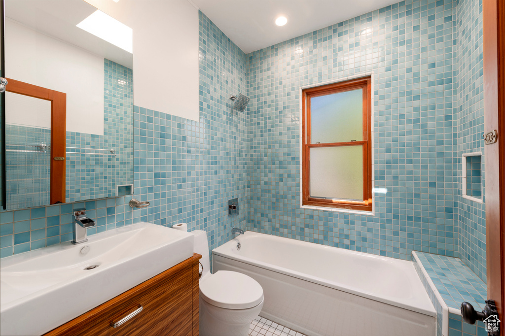 Full bathroom featuring tile walls, washtub / shower combination, toilet, tile patterned floors, and vanity