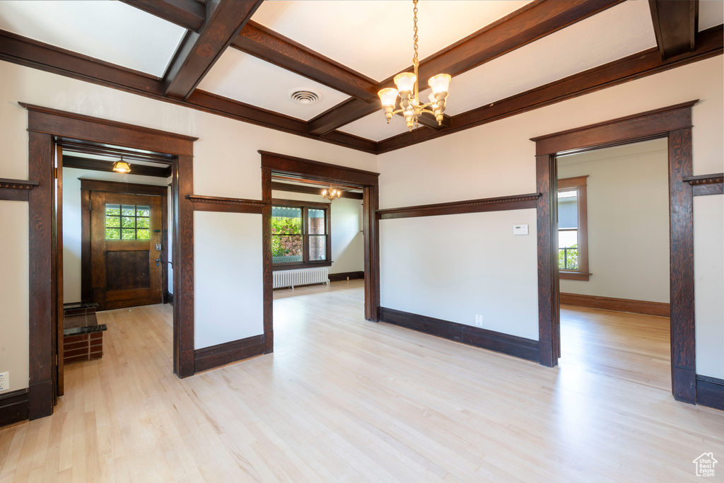Empty room with a chandelier, radiator heating unit, light wood-style flooring, baseboards, and coffered ceiling