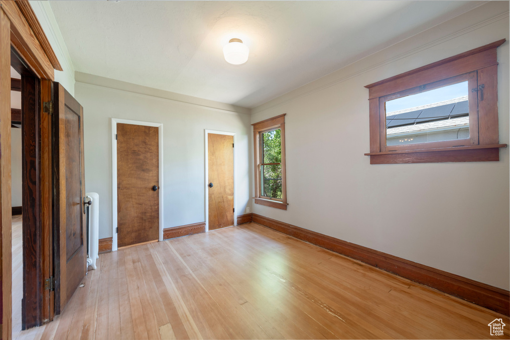 Unfurnished bedroom featuring baseboards, light wood-style flooring, radiator, and crown molding