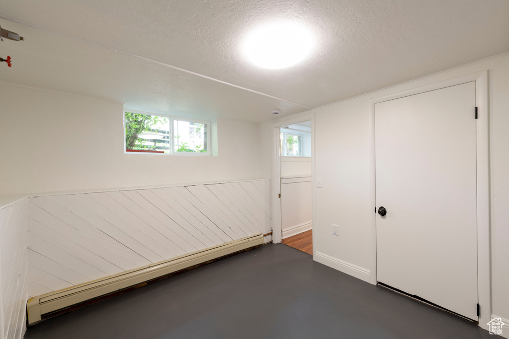 Below grade area with a baseboard radiator, a textured ceiling, and baseboards