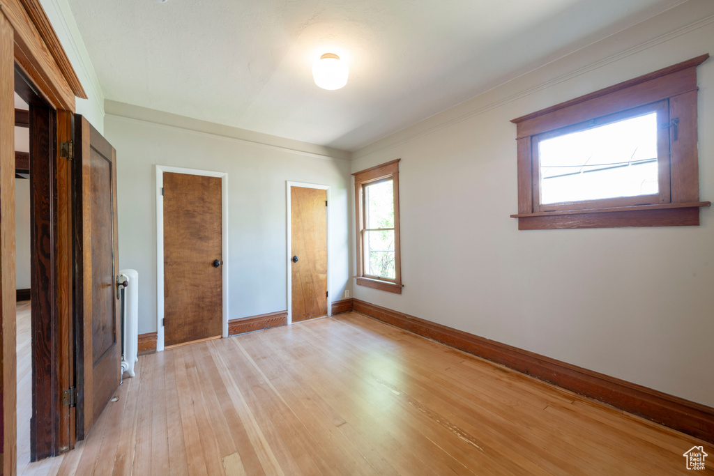 Unfurnished bedroom featuring baseboards, light wood-type flooring, radiator, and crown molding