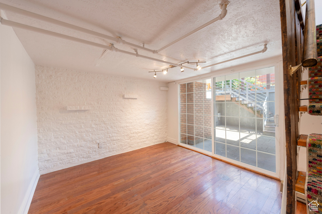 Spare room with brick wall, wood finished floors, baseboards, and a textured ceiling