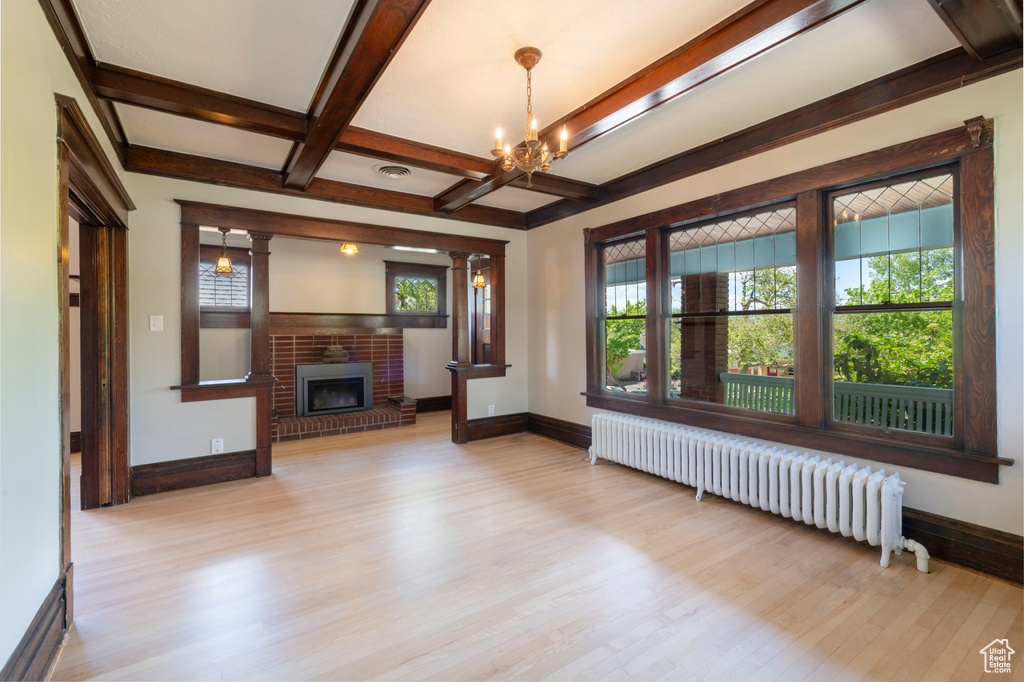 Unfurnished living room featuring radiator heating unit, a brick fireplace, baseboards, a chandelier, and wood finished floors