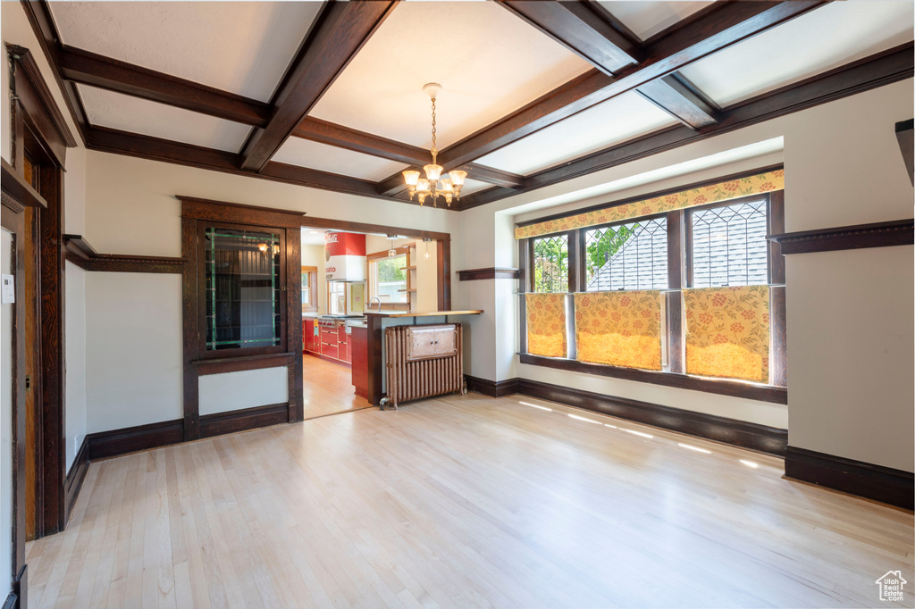 Unfurnished room with a chandelier, baseboards, coffered ceiling, wood finished floors, and beamed ceiling