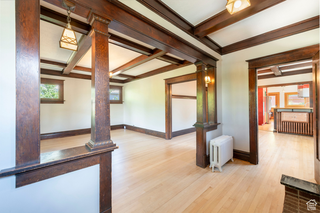 Empty room with radiator, ornate columns, beamed ceiling, baseboards, and wood finished floors