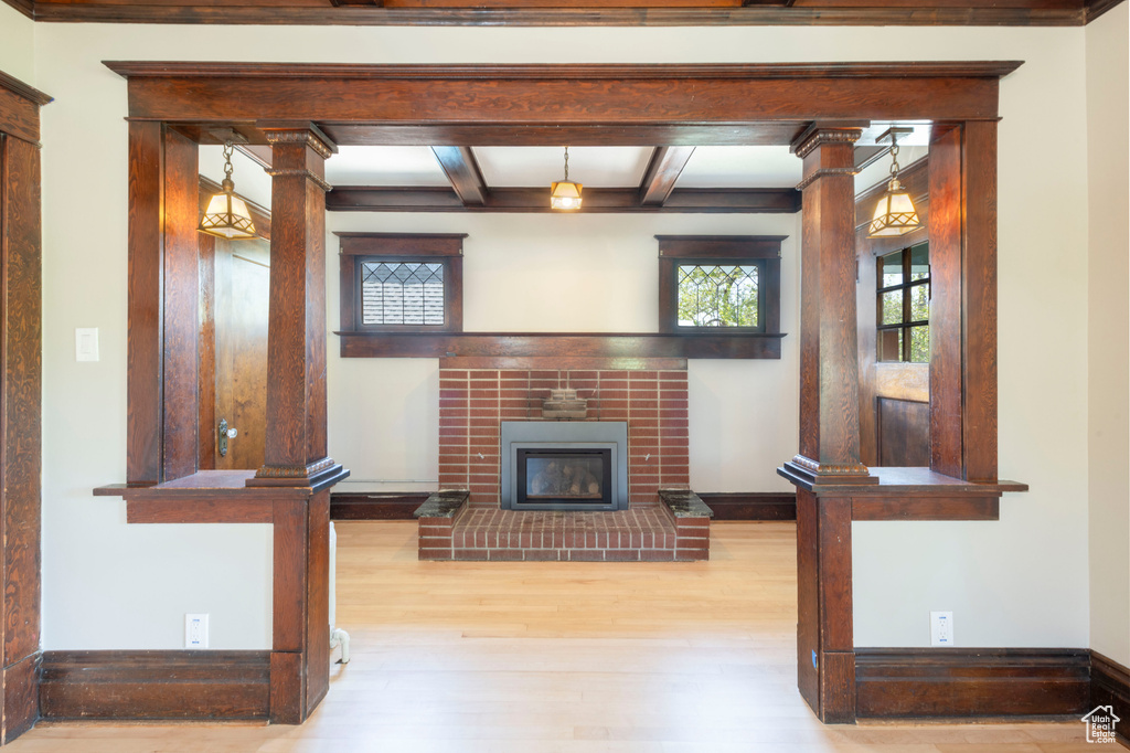 Unfurnished living room featuring wood finished floors, beamed ceiling, baseboards, a brick fireplace, and ornate columns