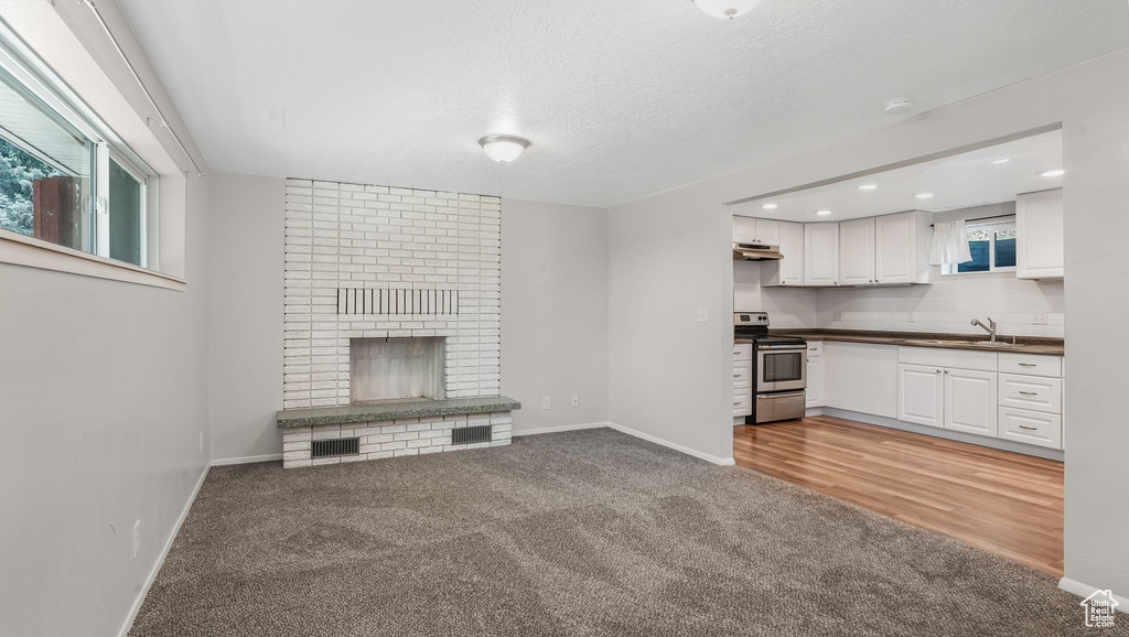 Unfurnished living room featuring light carpet, a sink, a fireplace, baseboards, and recessed lighting