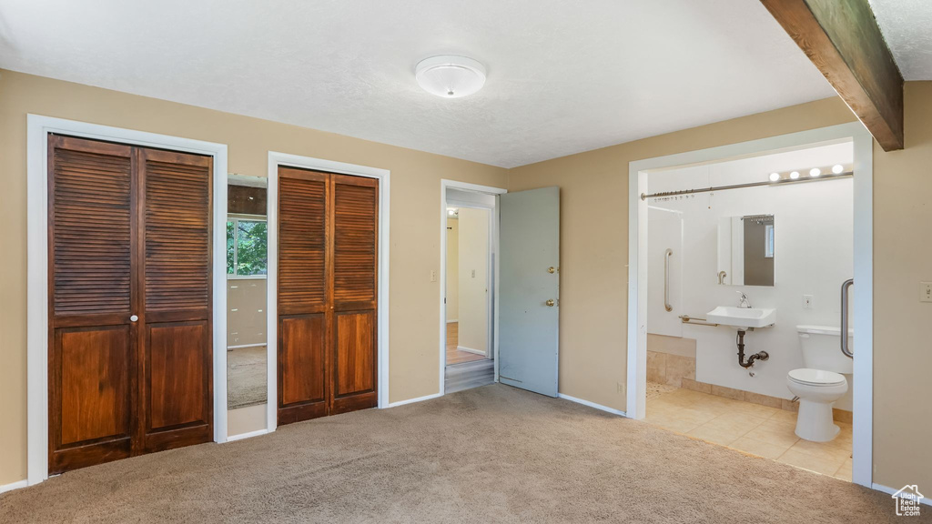 Unfurnished bedroom featuring multiple closets, carpet flooring, a sink, baseboards, and ensuite bathroom