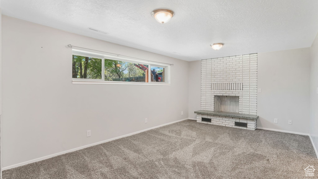 Unfurnished living room with a textured ceiling, a brick fireplace, carpet floors, and baseboards