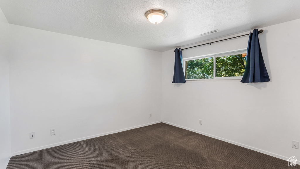 Unfurnished room with a textured ceiling, baseboards, and dark colored carpet