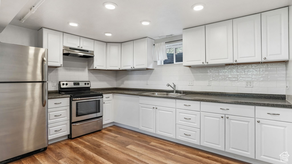 Kitchen with appliances with stainless steel finishes, a sink, under cabinet range hood, dark countertops, and recessed lighting