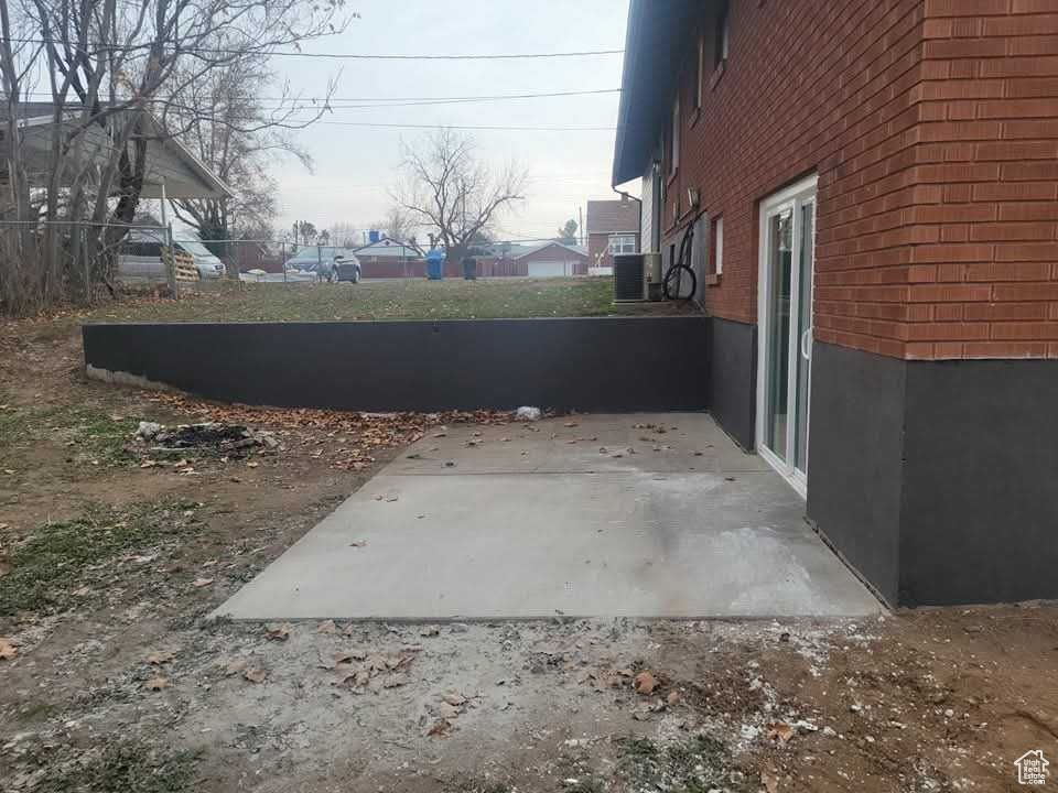 View of side of home with brick siding, a patio area, and central AC