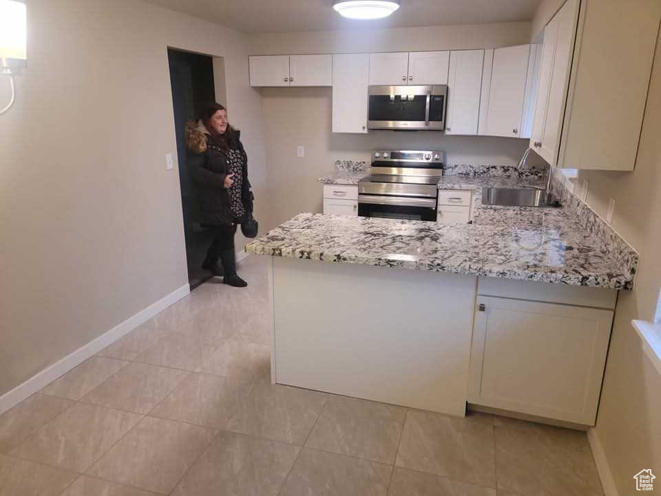 Kitchen featuring stainless steel appliances, light stone countertops, baseboards, a peninsula, and white cabinetry
